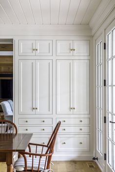 a kitchen with white cabinets and wooden chairs in the center, along with hardwood flooring