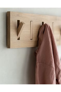 a wooden coat rack with hooks and clothes hanging on the wall next to a pink shirt