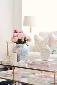 a coffee table with flowers and books on it in front of a white couches