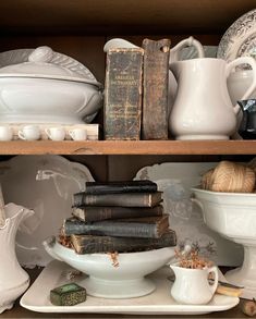 some books are sitting on top of plates in a shelf next to other dishes and vases