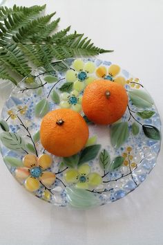 two oranges on a plate with leaves and flowers