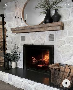 a fireplace with a fire in it next to two vases and a mirror on the wall