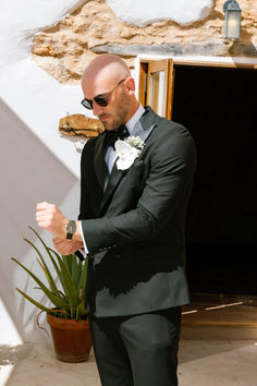 a man in a tuxedo and sunglasses standing next to a potted plant