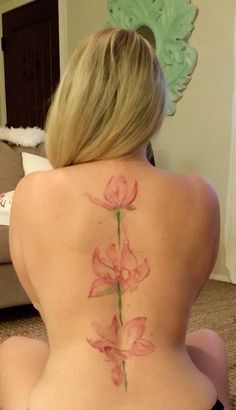 a woman sitting on the floor with her back turned to the camera and showing off her pink flower tattoo