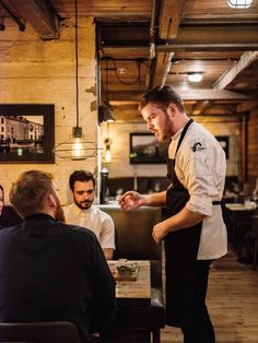 a man standing in front of a table with some food on it and people sitting around