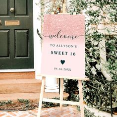 a welcome sign sitting in front of a door with greenery on the side walk