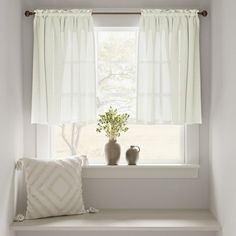 two vases sit on a window sill next to a pillow and potted plant