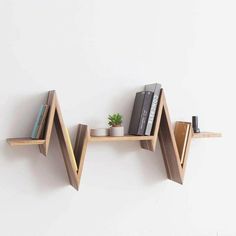 two wooden shelves with books on them against a white wall next to a potted plant