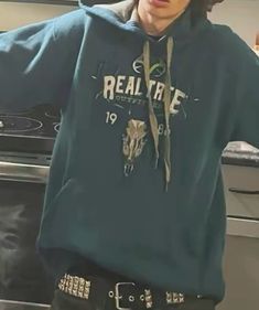 a young man wearing a green hoodie standing in front of a stove with his hands on his hips