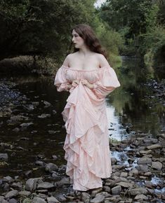 a woman in a pink dress standing on rocks near water