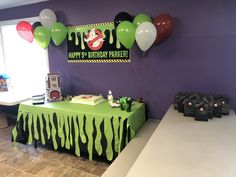 a birthday party with balloons and decorations on the table in front of a purple wall