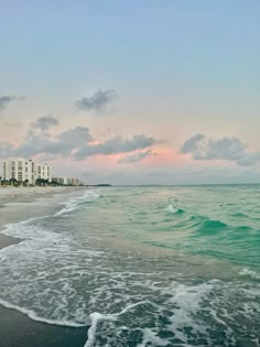 the beach is empty and has waves coming in from the ocean, with hotels in the background