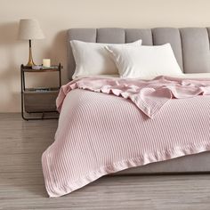 a bed with white sheets and pillows in a neutral colored room, next to a night stand