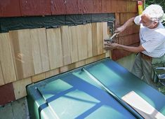 an older man is painting the side of a house with wood siding and green paint