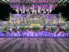 an elaborate floral display with purple flowers and greenery on the stage at a wedding reception