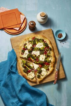 a pizza sitting on top of a wooden cutting board next to a knife and napkin