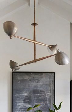 a modern light fixture hanging from the ceiling in a living room with potted plants