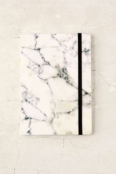 a white marbled notebook with black lines on the front and bottom, sitting against a wall