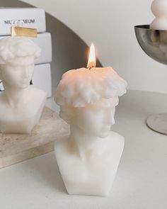 a candle that is on top of a table next to a busturine with a burning candle in it