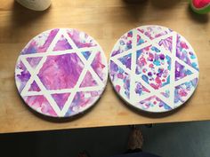 two painted plates sitting on top of a wooden table next to a person's hand