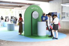 people are standing in front of a green and white booth at an art exhibition,