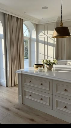 a large kitchen with white cabinets and an island in the middle is lit by a gold pendant light