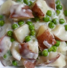 a white plate topped with peas and ham covered in cheese sauce on top of potatoes