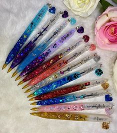 there are many different colored pens on the white surface next to some flowers and a rose