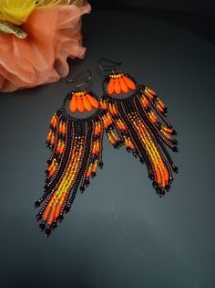 two pairs of orange and black beaded earrings on a table next to a flower