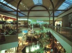 the inside of a mall filled with lots of plants and people walking around it at night