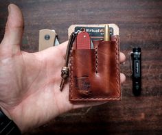 a hand holding a brown leather wallet with a pen and lighter in it on a wooden table