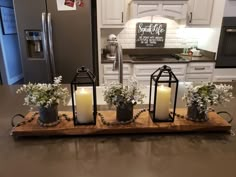 three candles are sitting on a wooden tray with flowers and plants in front of the refrigerator