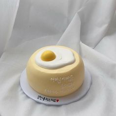 a yellow cake with an egg on top sitting on a white cloth covered tablecloth