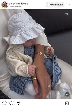 a woman holding a baby wearing a white hat and blue jeans on top of a couch