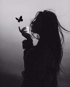 a black and white photo of a woman with long hair holding a butterfly in her hand