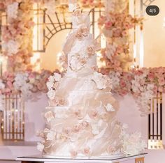 a white wedding cake sitting on top of a table in front of a floral wall