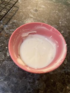 a pink bowl filled with yogurt sitting on top of a counter next to a cooling rack