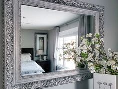 a large silver framed mirror sitting on top of a table next to a vase with flowers