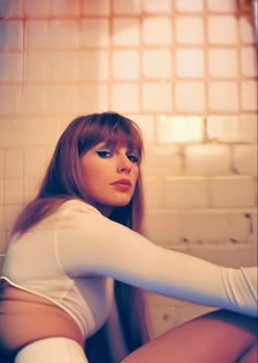 a woman with long red hair sitting on the floor in front of a tiled wall