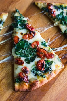 several slices of pizza with tomatoes and spinach on them sitting on a cutting board