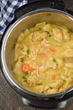 a pot filled with pasta and carrots on top of a wooden table next to a blue checkered napkin