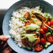 a person holding a plate with rice, tomatoes and avocado