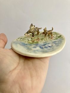 a miniature figurine of three dogs on a plate in the palm of a hand