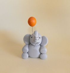 an elephant toy sitting on top of a table with an orange balloon attached to it's head