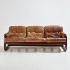 a brown leather couch sitting on top of a white floor next to a wooden frame