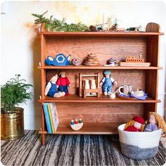 a wooden shelf filled with toys next to a potted plant