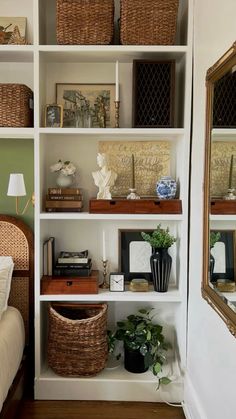 a white book shelf filled with lots of books and other items next to a bed