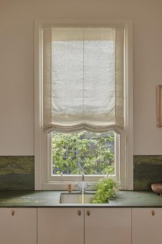 a kitchen window with roman shades over the sink and counter top, in front of an open window