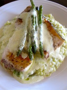 a white plate topped with chicken and asparagus covered in gravy on top of mashed potatoes