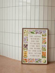 a white tiled wall next to a wooden table with a framed print on it that says the grass, flowers, and hearts